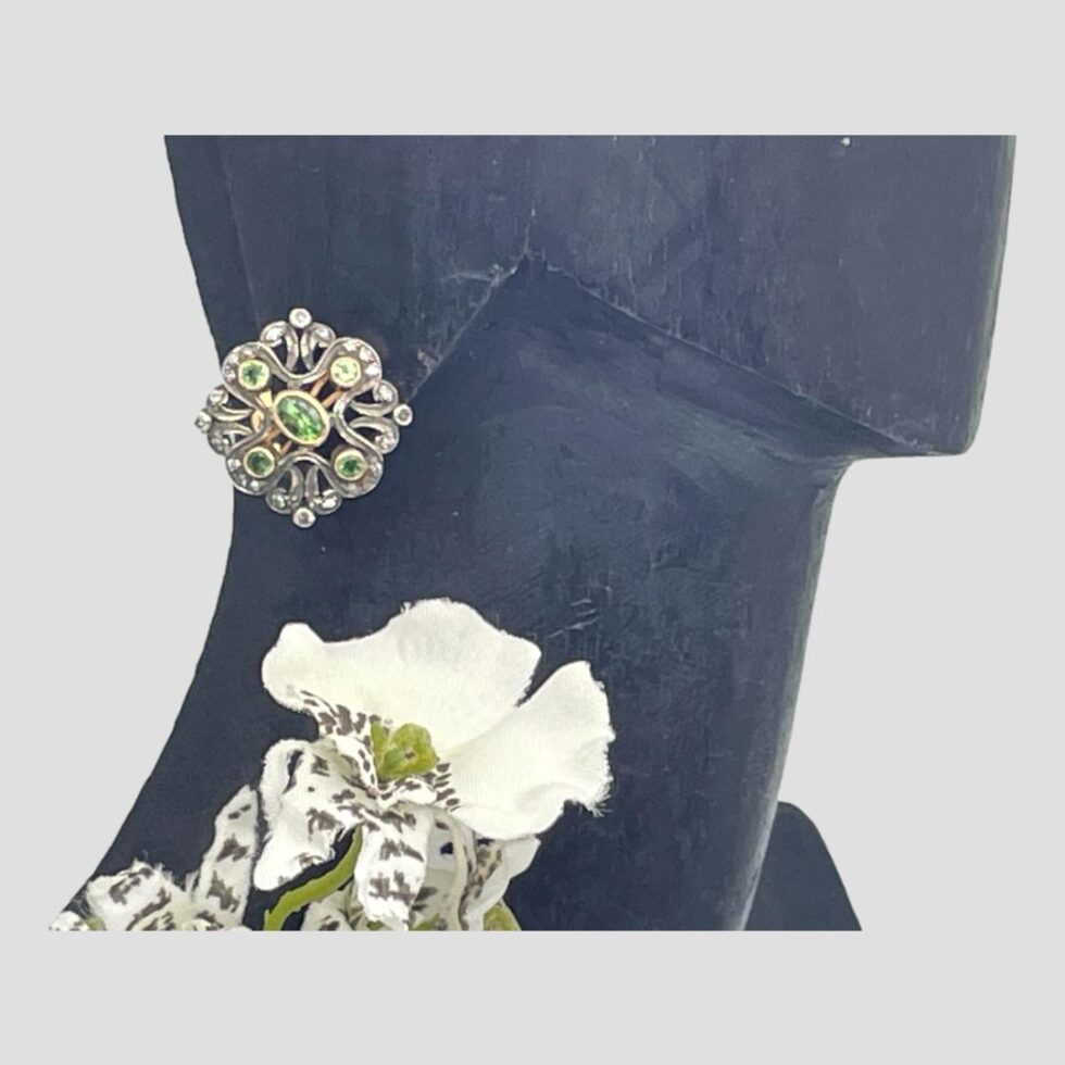 Photo of one peridot diamond stud displayed on a dark wooden display stand with the earring in the ear lobe. It has been positioned at diamond angle rather than square. A fraction of faux white orchid is visible below for display only.