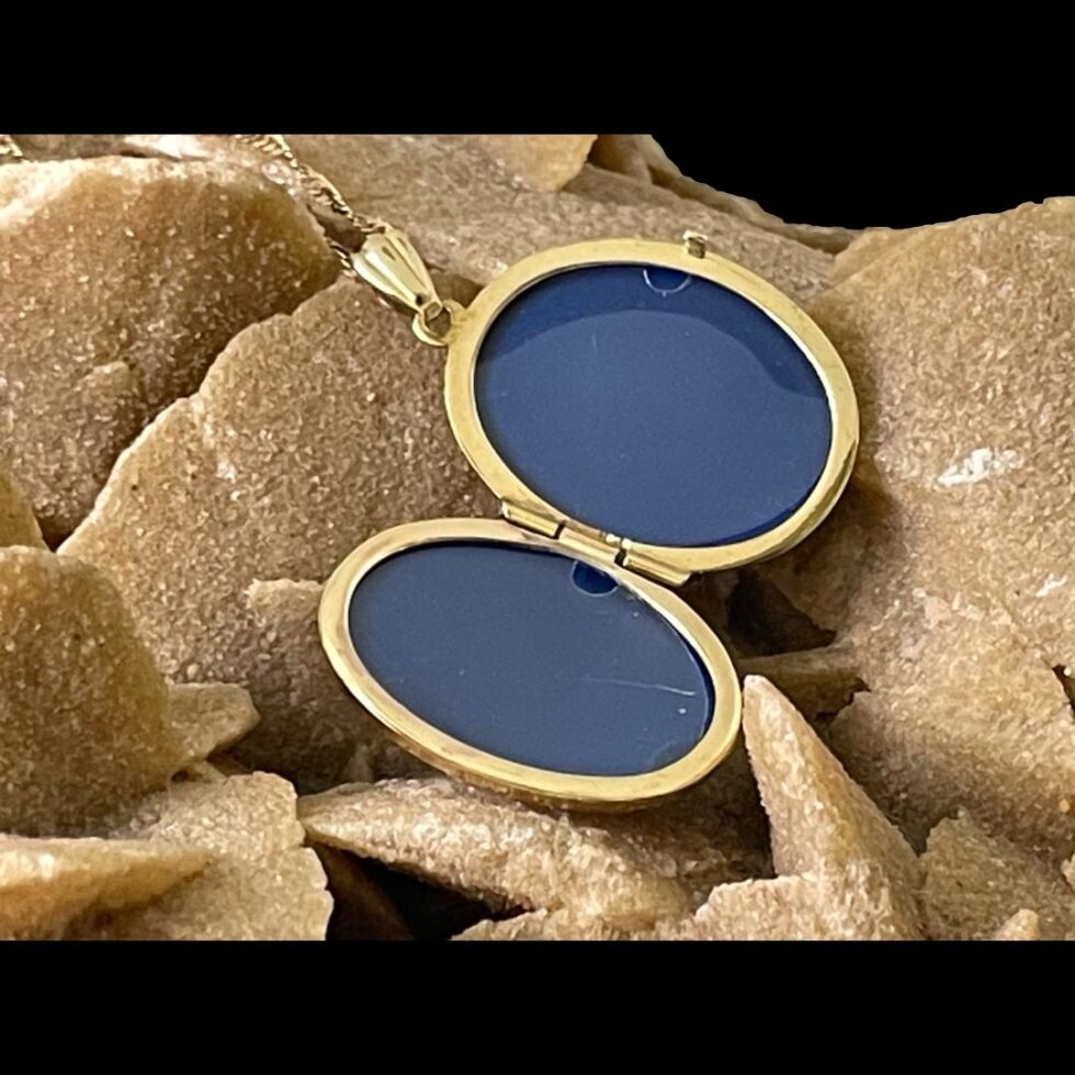 Photo of 9kt gold cameo locket displayed on a rock and shown open. The cameo has a blue interior covered in clear plastic to protect photos/hair.