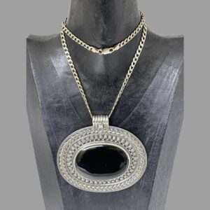Main photo of large onyx pendant &chain displayed on a black wooden display stand and facing forward. The chain is fairly long so has been wound round once around the neck. The large pendant covers almost all of the chest of the stand. It is ovular in shape with the shorter ends to left and right. An incredible statement piece which will get you noticed. A thick snake chain may be more compatible with this pendant depending on how and where you would like it to hang on your person!