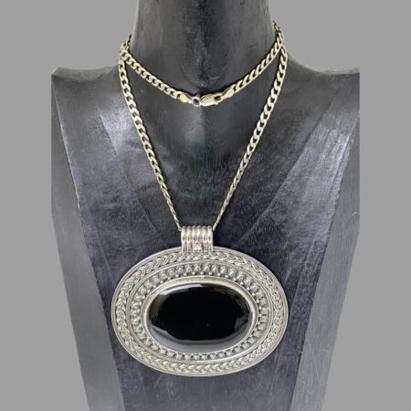 Main photo of large onyx pendant &chain displayed on a black wooden display stand and facing forward. The chain is fairly long so has been wound round once around the neck. The large pendant covers almost all of the chest of the stand. It is ovular in shape with the shorter ends to left and right. An incredible statement piece which will get you noticed. A thick snake chain may be more compatible with this pendant depending on how and where you would like it to hang on your person!