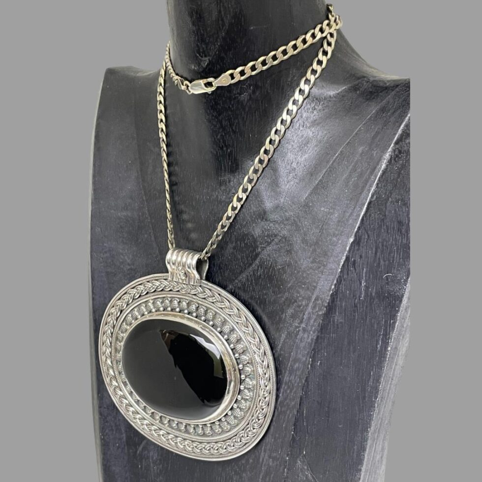 Photo of large onyx pendant &chain still displayed on a black wooden display stand this time with the pendant facing the bottom left corner.