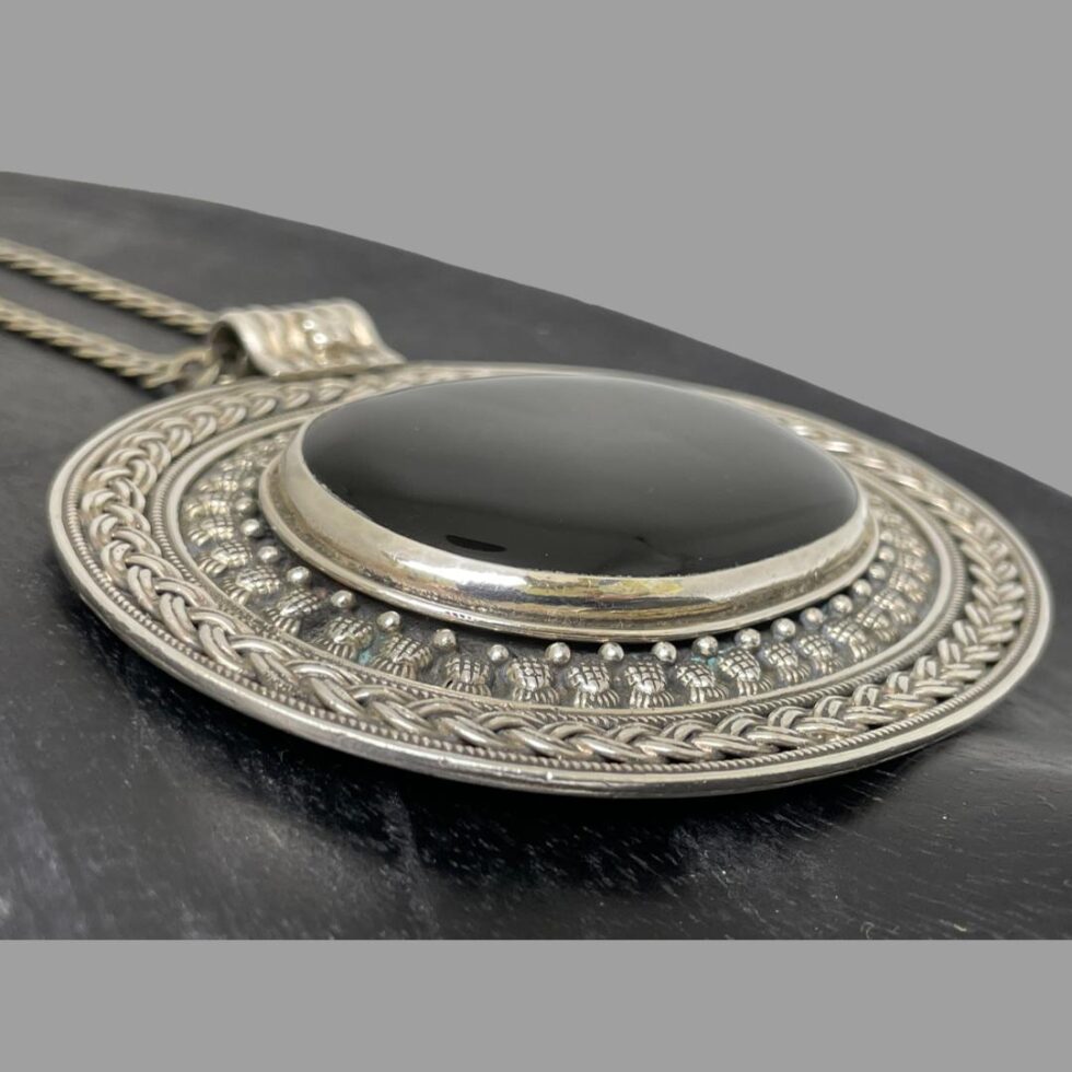 Close up of the pendant seen from a slight side angle to show the depth and size of the black onyx. It is set in its own silver frame slightly above the rest of the large pendant.