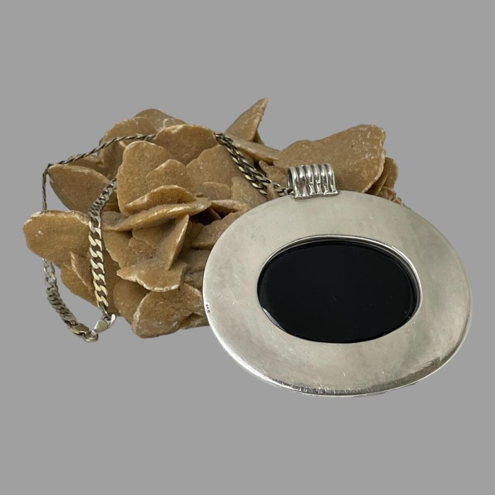 Photo of pendant displayed from the back. It is leaning against the rock of desert sand rose. The tiny hallmark of 925 is visible just to the left.