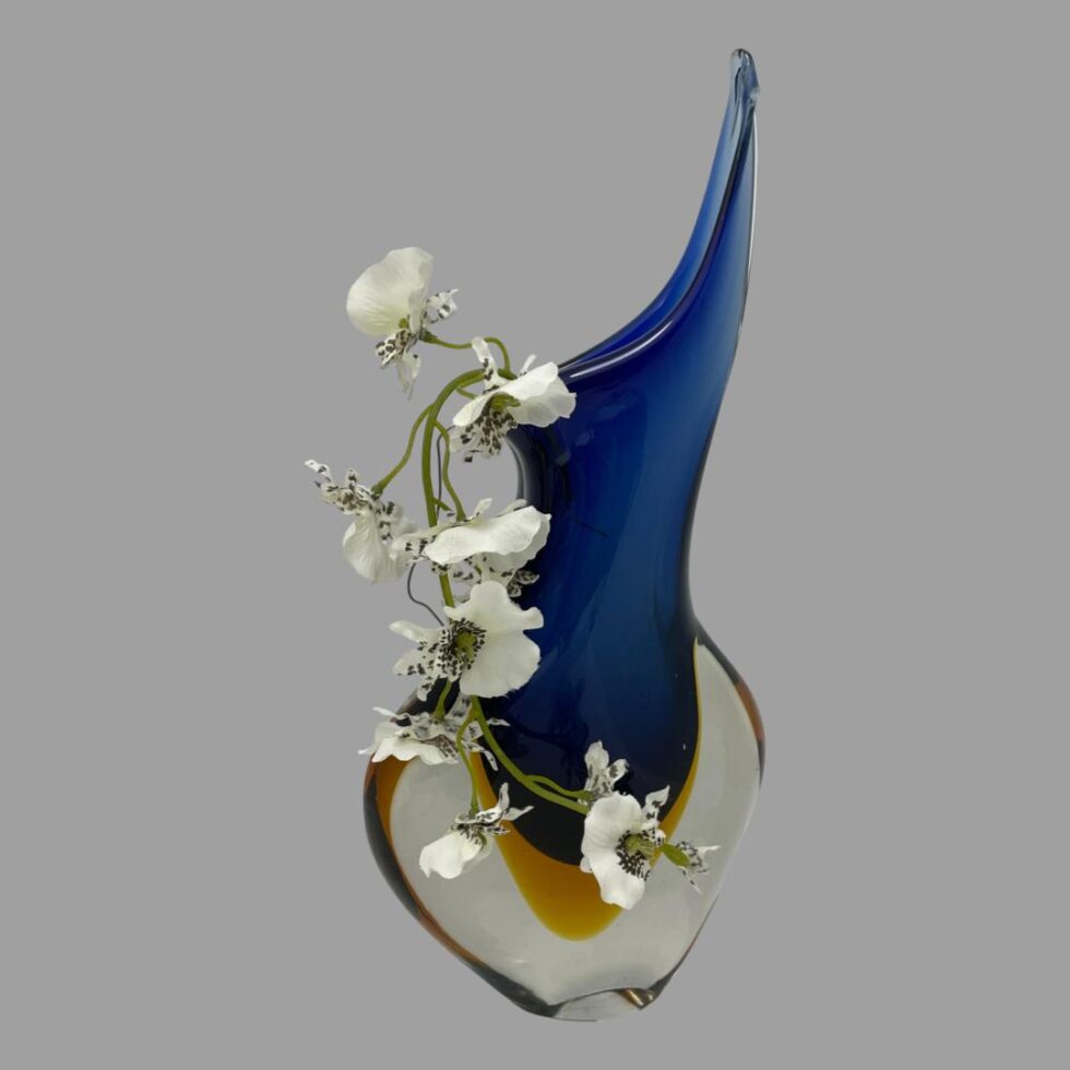 Photo of Murano blue sommerso vase again from a wide side angle this time with the extended lip at the top on the right and a spray of white orchids cascading down to the left.