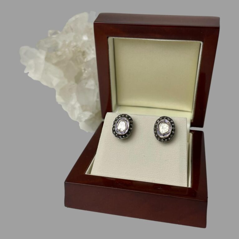 Main photo of rose cut diamond studs displayed inside their box and forward facing. To the centre of each earring there is a large rose cut diamond with its own silver frame. The blue enamel area is visible followed by outer circle of 16 smaller diamonds. The centre diamond gives a stunning shine. The box is a mahogany like wood with a cream interior. There is a rock of natural quartz crystal protruding from the left of the open box.