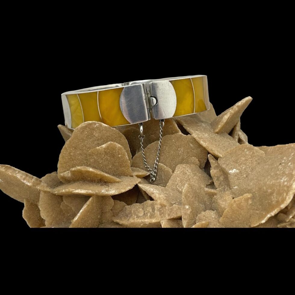 Main photo of Modernist silver amber bracelet displayed on top of a rock of natural desert rose with the clasp section in the foreground. The amber pieces are in sections of different egg yolk amber shades which appear to be graduating in colour.