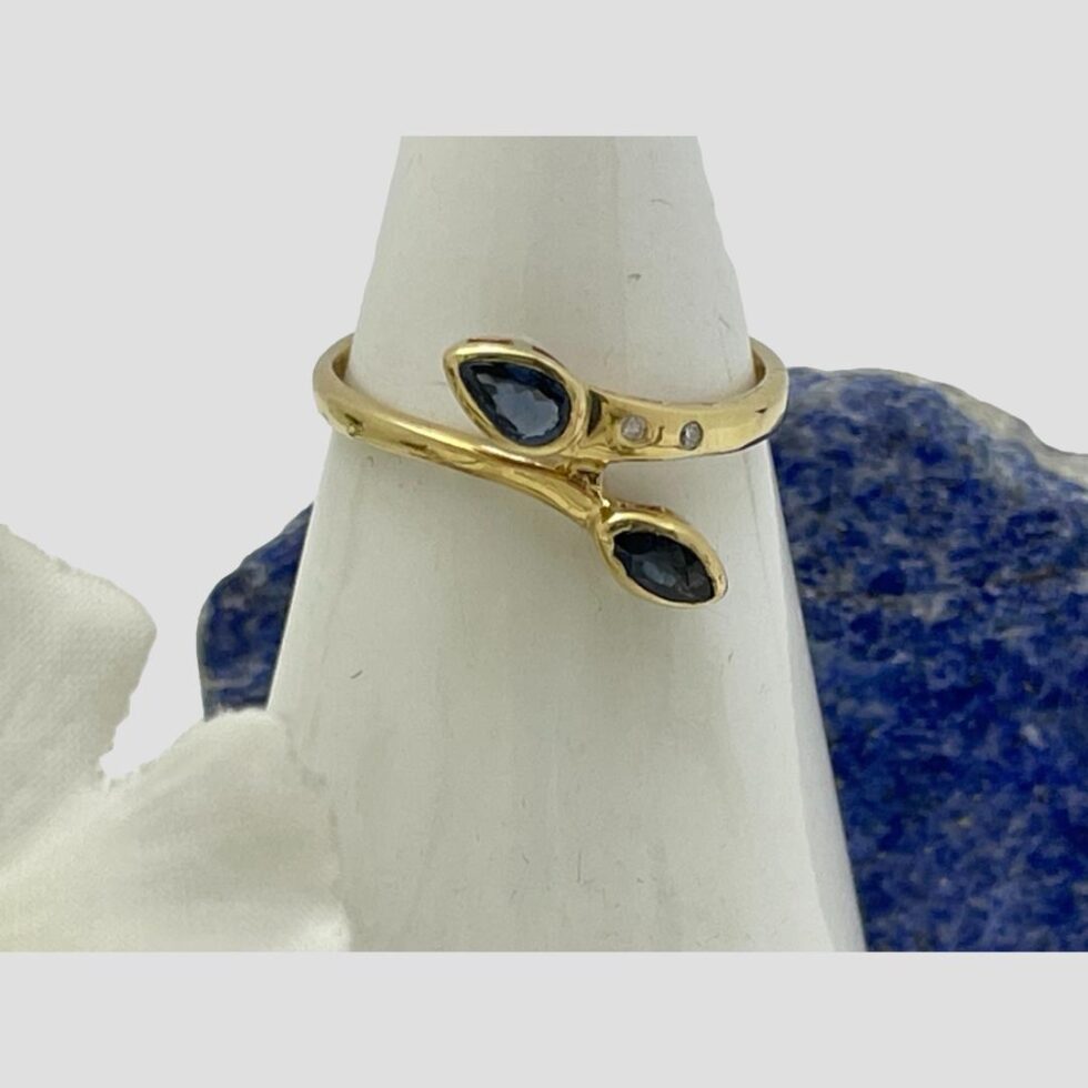 Photo of gold sapphire diamond ring this time displayed on a cone shaped stand with the ring front forward facing. The rock of lapis is now behind the ring.