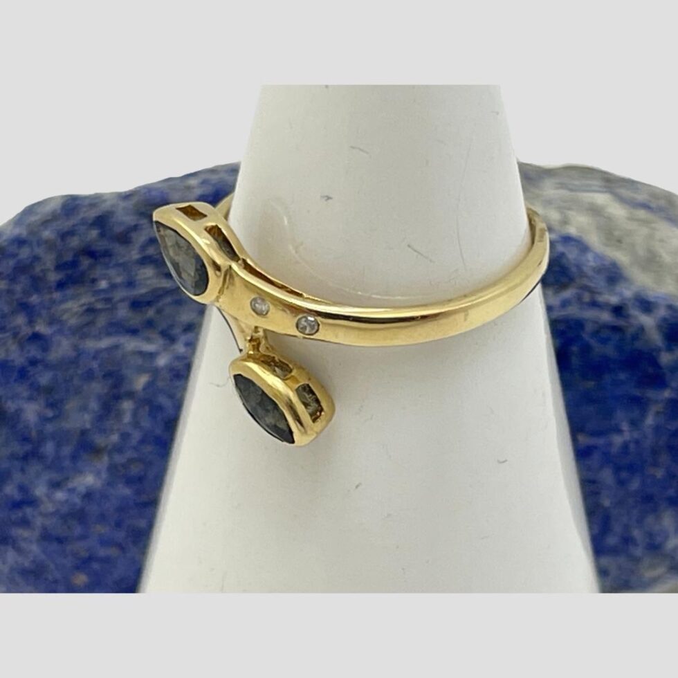 Photo of ring still displayed on a cone shaped stand with the ring front facing to the bottom left corner. The shot is slightly raised so we are looking down a little at the ring. The diamonds are visible well and the drop cut sapphire below them on the split band.