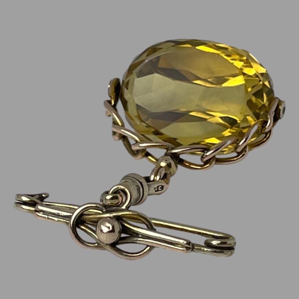 Photo of gold citrine fob laid flat with the citrine in the top right corner and pin in the bottom left..