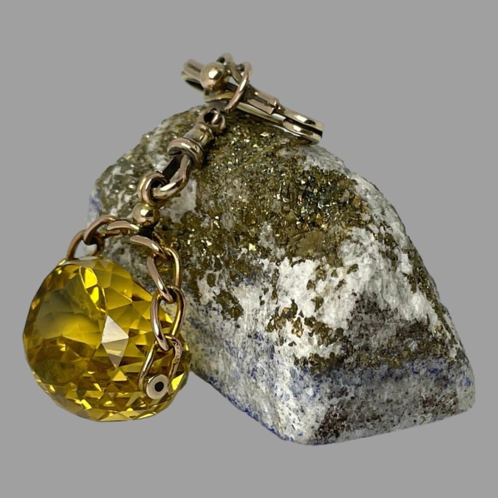 Photo of antique gold citrine fob still displayed in same pose as main photo but this time seen from a side view with the flat at the front of stone facing the bottom left. The pin is still resting on the lapis rock. From this angle, it is possible to view the incredible facet work on the citrine stone.