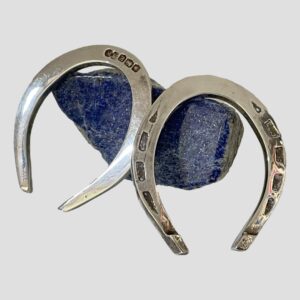 Main photo of both horseshoes displayed outside of the case and leaning against a small rock of lapis lazuli. The shoe on the right is displaying the nail holes and one on left shows hallmark. Both shoes are displayed the correct way up ie; with opening end at bottom to 'let the luck flow' The fitted case also houses shoes the 'right way up'