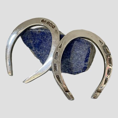 Main photo of both horseshoes displayed outside of the case and leaning against a small rock of lapis lazuli. The shoe on the right is displaying the nail holes and one on left shows hallmark. Both shoes are displayed the correct way up ie; with opening end at bottom to 'let the luck flow' The fitted case also houses shoes the 'right way up'