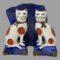Main photo of Staffordshire Potteries seated cats posed in front of a rock of natural lapis lazuli and facing forward. The blue of the stone is almost identical to the blue of the cats cushions. The cats are off white in colour with dark terracotta spots and both have a golden brown ribbon around the neck.