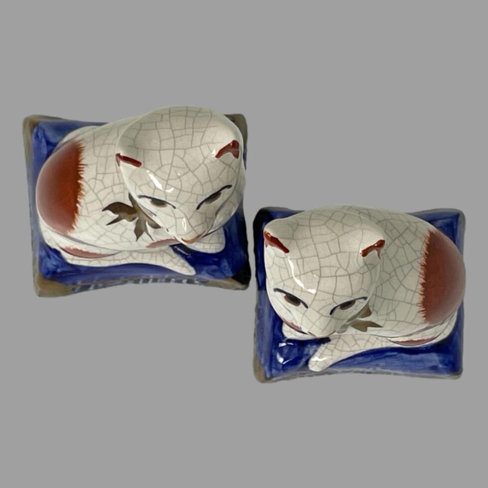 Photo of both Staffordshire cats looking straight down from above. One cat is slightly lower than other.