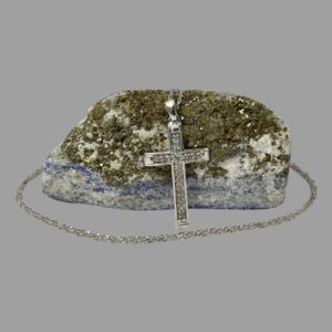 Main photo of gold diamond cross &chain displayed with cross leaning against a rock of lapis with mostly gold ore visible. The white gold diamond encrusted cross is seen forward facing. The chain extends over the top of rock of lapis and circles round the front.