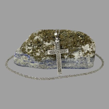 Main photo of gold diamond cross &chain displayed with cross leaning against a rock of lapis with mostly gold ore visible. The white gold diamond encrusted cross is seen forward facing. The chain extends over the top of rock of lapis and circles round the front.