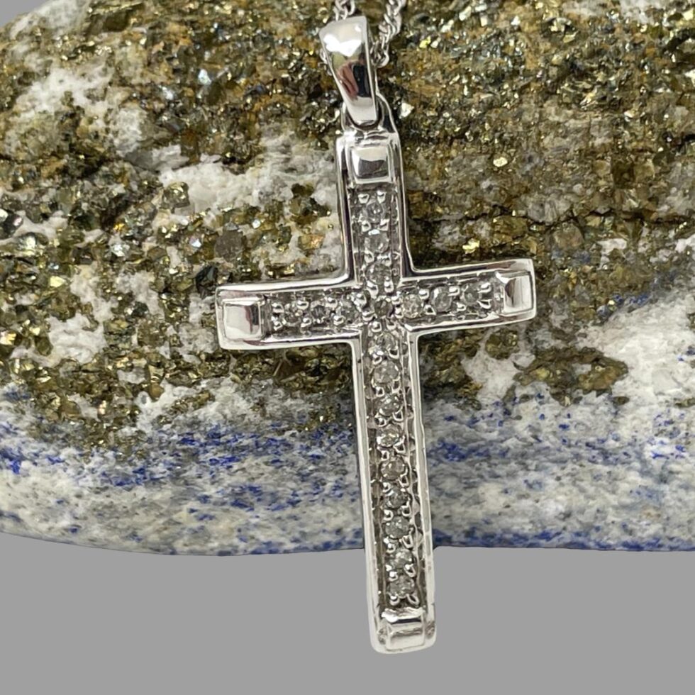 Close up photo of the diamond encrusted white gold cross still leaning against rock of natural lapis gold ore and front forward facing.
