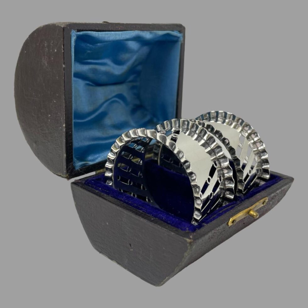 Photo of the silver napkin rings still displayed inside their fitted case with the open mouth facing towards the bottom right corner.