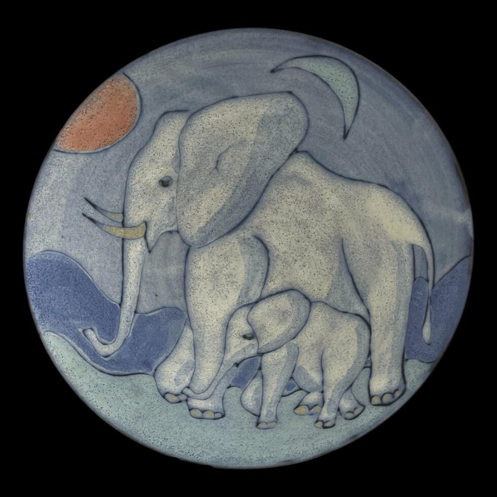 Main photo of elephants bowl Tessa Fuchs looking straight down into the whole detail in the bowl centre of the elephants adorning this piece of amazing studio art. The sun is red and to the top left and crescent moon is blue and to the top right. The elephants are facing left towards the red sun. The elephants are a pale grey blue with blue areas to highlight the shadows. The adult elephant takes up quite a large portion of the picture. The calf walks beside the adult in the foreground and fits between its front and back legs. The ground, mountain range in background and sky are different shades of blue - the darkest being the mountain range.