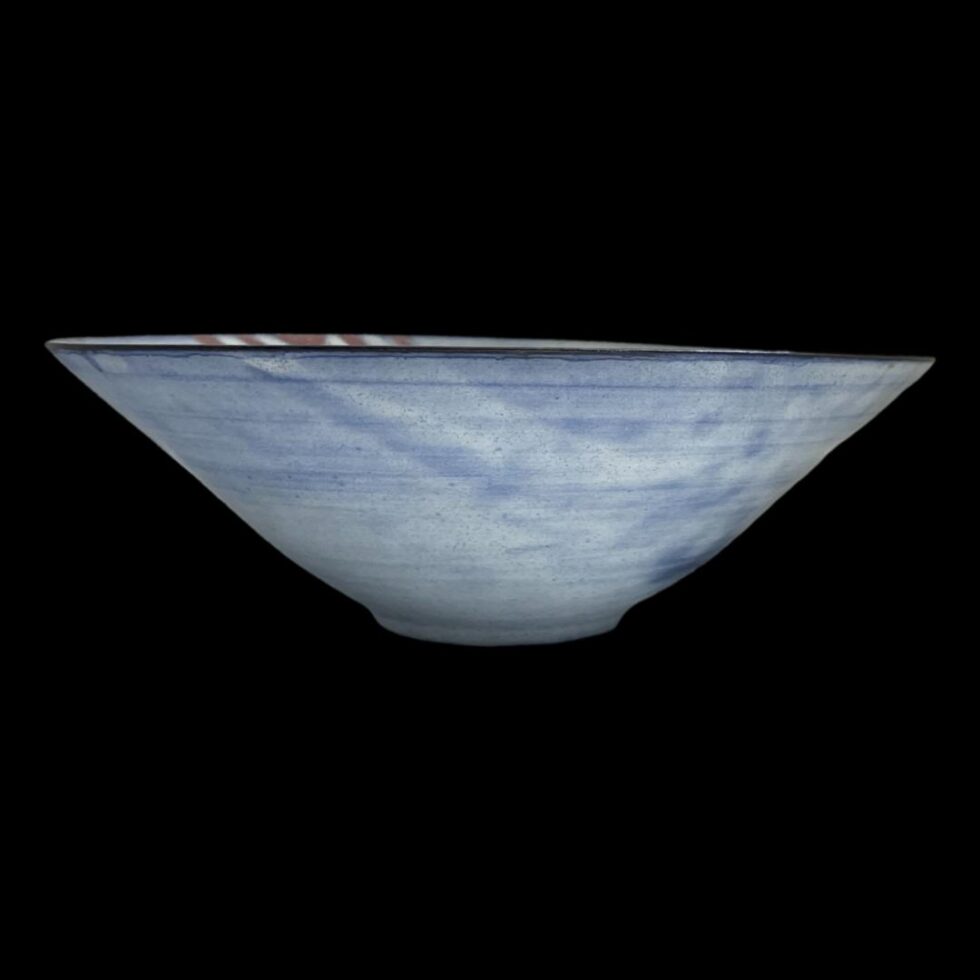 Photo of bowl seen from an eye level. The bowl has a wide cone shape and is a light blue with patches of slightly darker blue in the mix. Very striking against the black background.