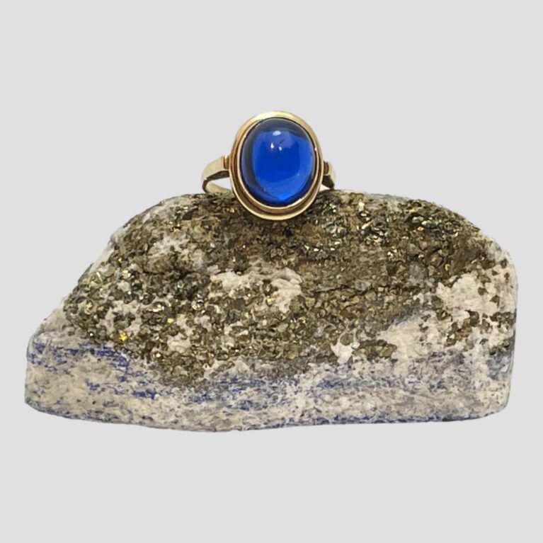 Main photo of gold &blue spinel ring displayed on top of a rock of natural lapis and seen with the ring front forward facing. The blue of the spinel is so striking that the gold setting requires no fancy details - the spinel itself does all the wowing! The gold detail is quite plain but does the job. A nice double frame setting at the front and sturdy at back. Plain band.