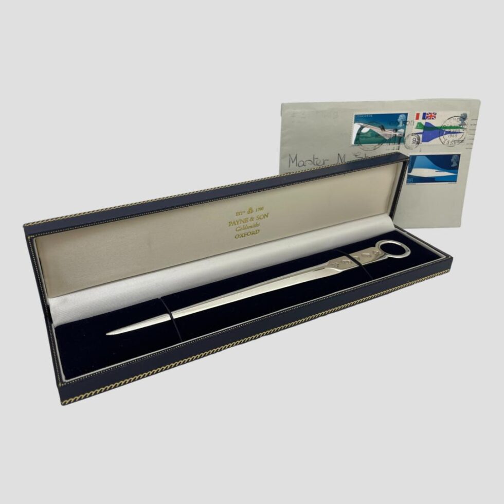 Main photo of cased silver letter opener displayed inside its original case. A long and slender sterling silver opener with a hole in the handle tip for finger or thumb tip. There is a vintage letter in the background with old Concorde stamps on in the background for display only.