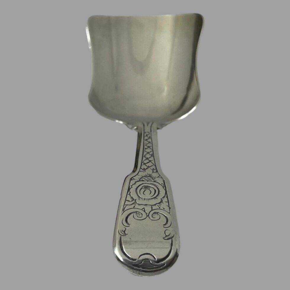 Photo of the tea caddy spoon laid vertically on a flat surface with the handle in the centre foreground.