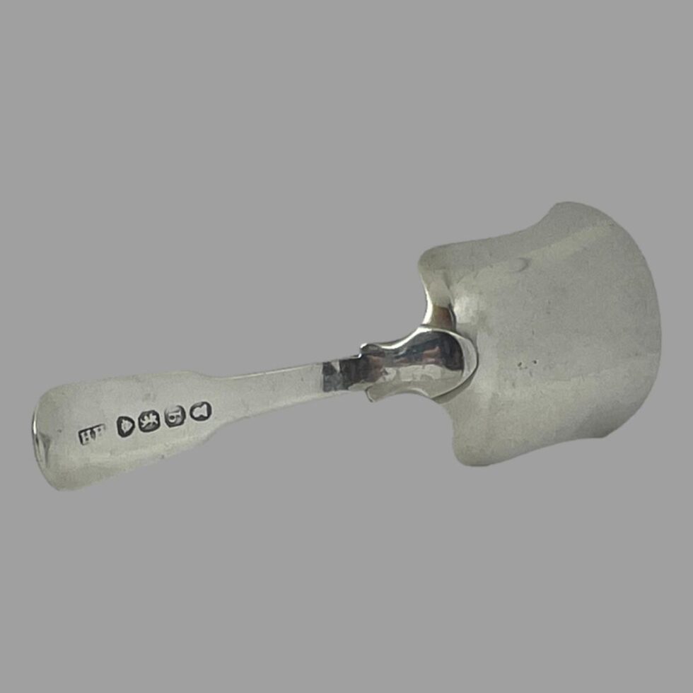 Photo of the back of antique tea caddy spoon displayed upright on its side. The hallmark is visible to the end of handle tip on the left.