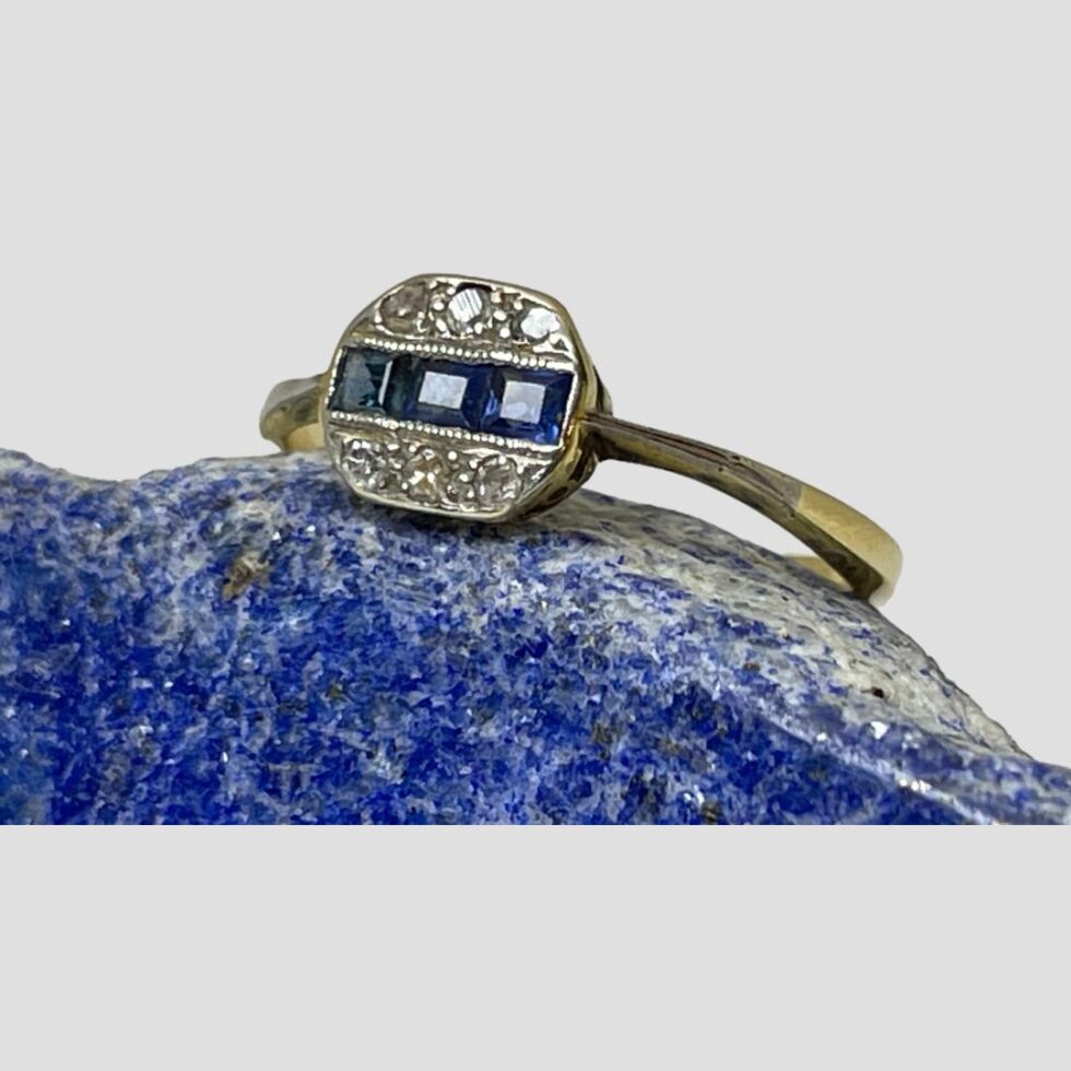 Photo of Deco sapphire diamond ring still displayed on a rock of lapis with the ring front facing to the upper left. The platinum overlay on the shoulder is visible.