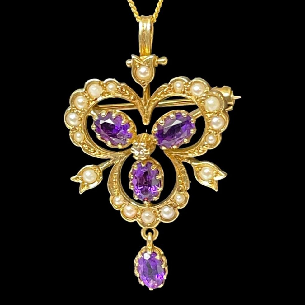 Photo of gold pendant brooch &chain displaying just the pendant/brooch against a black background. The light is shining on the piece this time and the amethysts are lit up a beautiful bright purple.