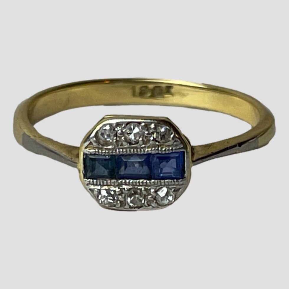 Photo of ring on a flat surface with ring front forward facing. The 18ct hallmark is visible to the inside band.