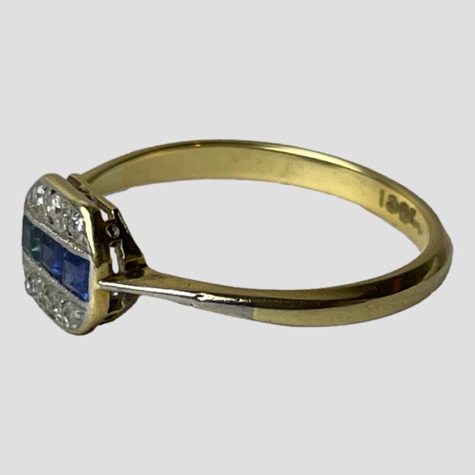 Photo of ring on a flat surface and seen with the ring front facing towards the bottom left corner. The hallmark is just visible on the inside of band on the right.