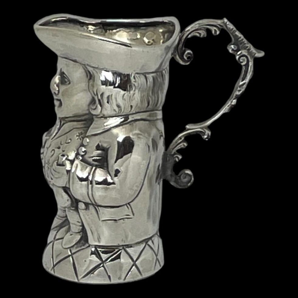 Photo of silver Toby Jug seen from a side angle with the front facing left. The lovely elaborate handle and thumb rest is well visible here.