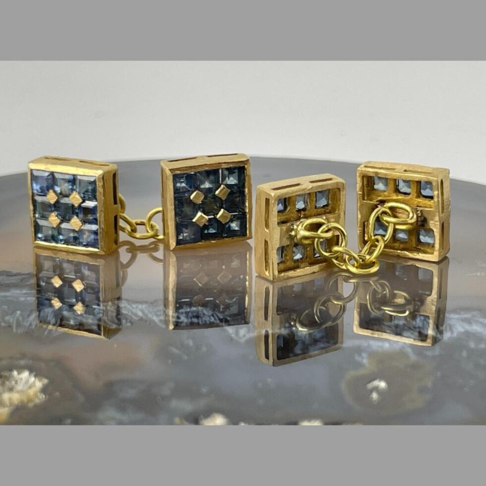 Photo of both cufflinks displayed stood upright on the slice of agate. The cufflinks on left are displayed with sapphire sides on show and the ones on right are displaying the backs and chain.