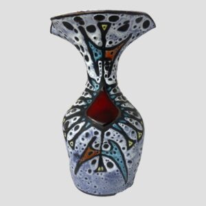 Main photo of Vallauris fat lava vase seen from an eye level with the most decorated side on display. The photo is taken at eye level to show the form of the vase clearly. It is bottle shaped but with a large wide fluted top. The top of the vase is actually wider than the bottom. The base colour is a light blue with white and speckled black 'lava' gaps throughout. All the colours are matt except for the cherry red diamond shape just below the slender neck. The matt colours include red yellow and turquoise all within black lava beading.