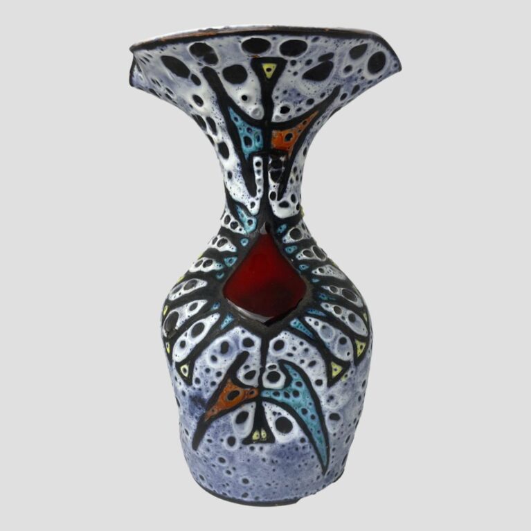 Main photo of Vallauris fat lava vase seen from an eye level with the most decorated side on display. The photo is taken at eye level to show the form of the vase clearly. It is bottle shaped but with a large wide fluted top. The top of the vase is actually wider than the bottom. The base colour is a light blue with white and speckled black 'lava' gaps throughout. All the colours are matt except for the cherry red diamond shape just below the slender neck. The matt colours include red yellow and turquoise all within black lava beading.