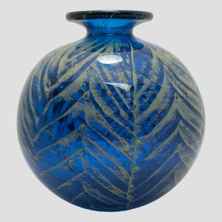 Main photo of signed Mdina ball vase seen from an eye level. The stunning lagoon blue vase has light golden palm like fronds shimmering over the top and all around giving a feeling of tropical paradise. The fabulous large ball shaped vase is finished with a modest lip at the top.
