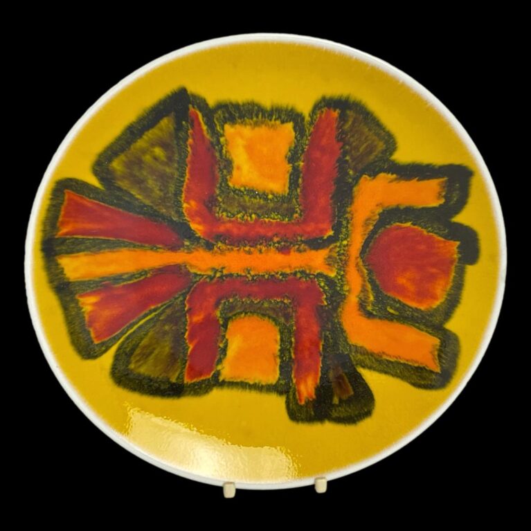 Main photo of Poole yellow Delphis dish displayed on a plate stand and against a black background. The abstract design to the centre in orange red and brown blocks of different shapes put together. To me looks like a person with arms raised in a dancing swirl.
