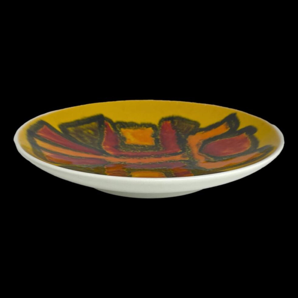 Photo of Poole yellow Delphis dish seen from a slightly raised angle from eye level looking diagonally down. The white base which also forms a frame around the dish front is visible and part of the yellow Delphis design.