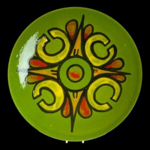 Main photo of large Poole Delphis dish displayed on a plate stand against a black background. The base colour of the dish is a beautiful young leaf green with a colourful design emanating from the centre in yellow, orange and red. There is a Mexican fiesta feel about the colouring and design of this piece.