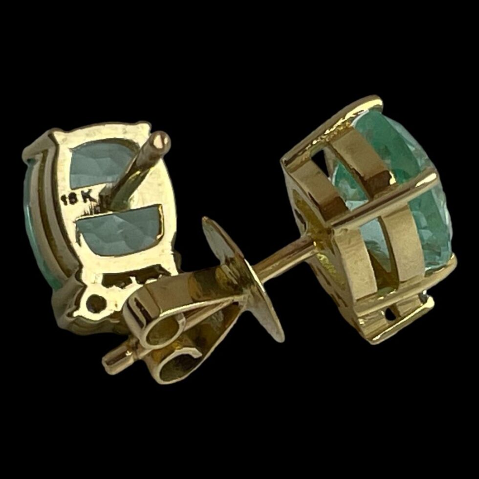 Photo of the earrings displayed against a black background with the one on left with butterfly removed and showing the 18k hallmark and one on right displayed from a side angle showing the gold setting for the emerald with butterfly in place. The butterflies have a generous flat disc which sits against the back of lobe which keeps the earring securely in place.