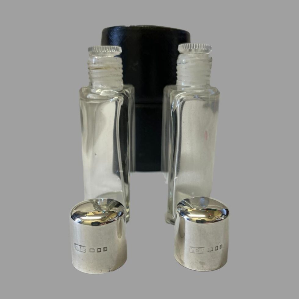 Photo from an almost eye level of the Deco silver topped bottles with case at back shown closed, bottles at centre with glass stoppers in place and silver tops in the foreground with their hallmarks on display.