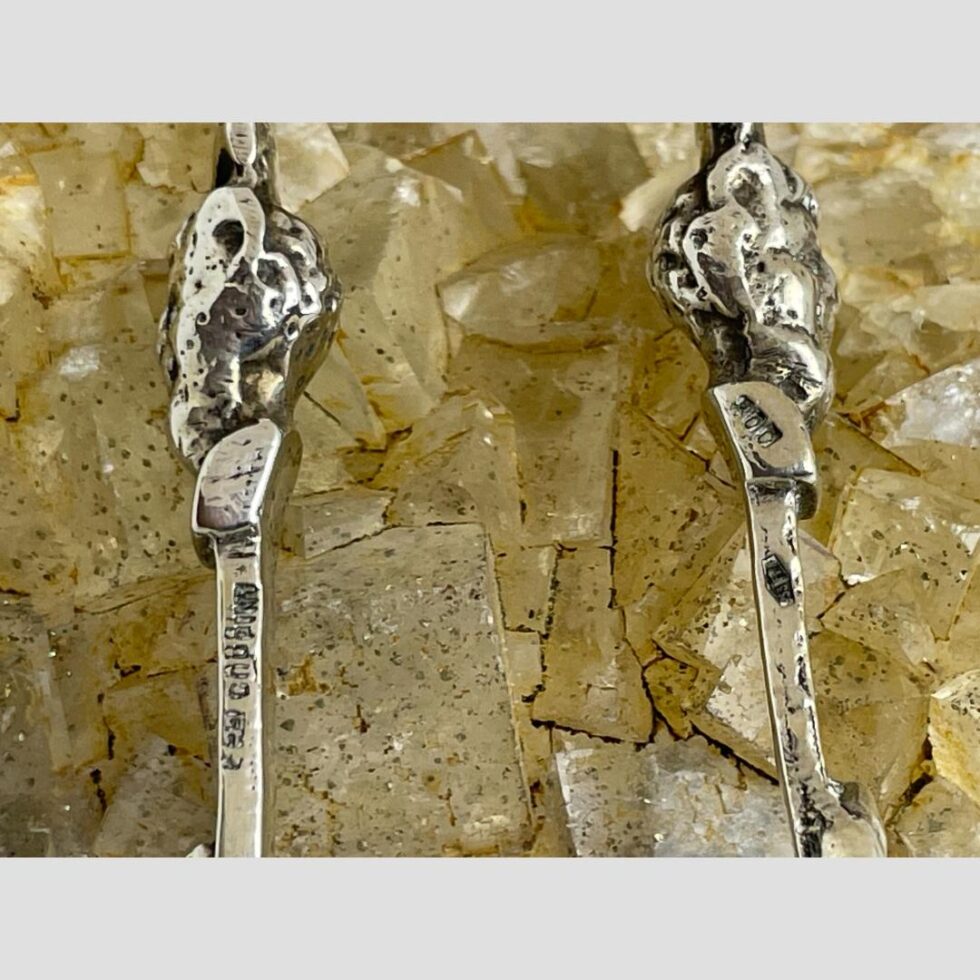 A close up photo of the devil like heads at the top of the tongs shown in profile. The hallmarks are visible to the left and right.