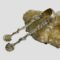 Main photo of Continental silver sugar tongs displayed leaning against a rock of river quartz and displayed with one side of the tongs in the foreground. Both sides are decorated the same with scallop spoon ends, a smooth snake entwined and crawling halfway up the tongs and finishing at the devil like heads at the top. The top of the tongs is plain silver.