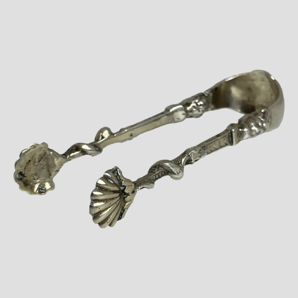 Photo of silver sugar tongs laid on a flat surface with the scallop ends in the left foreground.