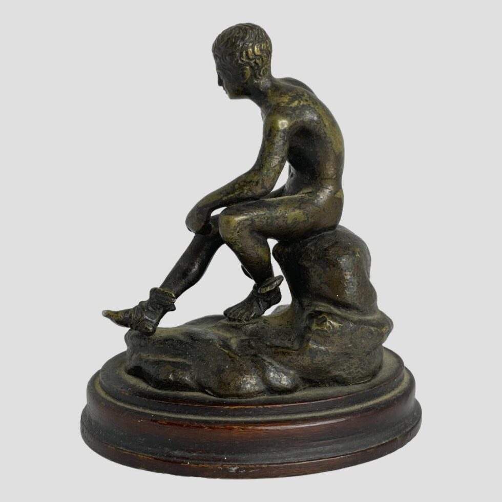 Photo of Hermes seen from a full on side angle. He is faced to the left and his left leg is in the foreground and bent at knee and pulled in with left arm rest of it.