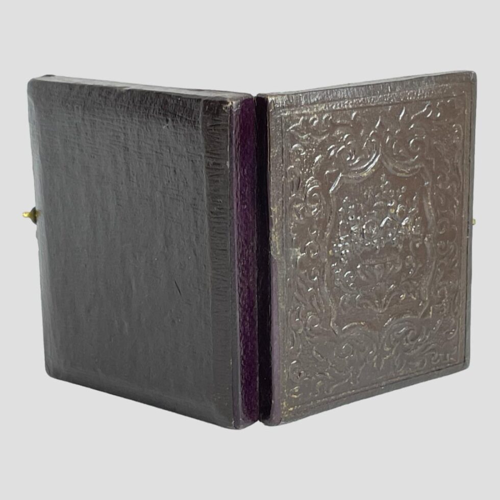 Photo of the daguerreotype shown open and upright seen from the leather cover side. The embossed leather cover is to the right and the back is smooth plain leather.