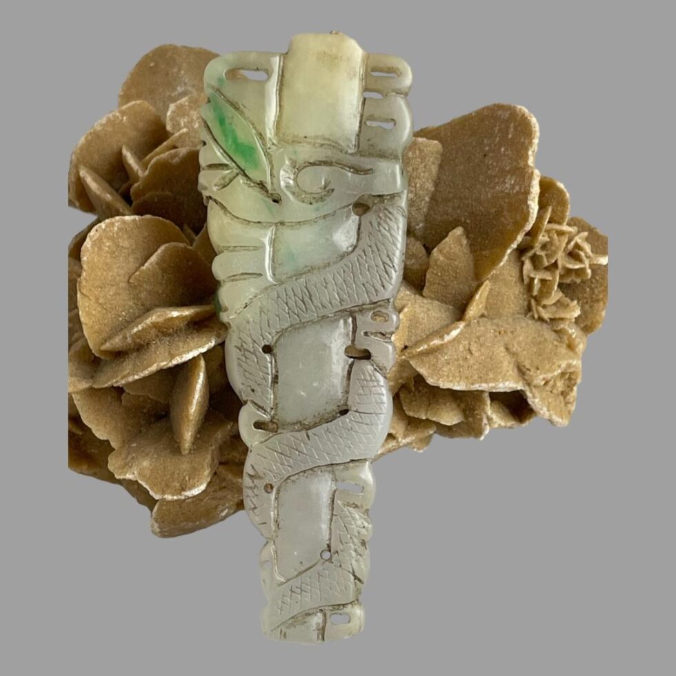Photo of the back of the long jade dragon pendant still leaning against the desert sand rose. Only one apple green jade area to the top left.