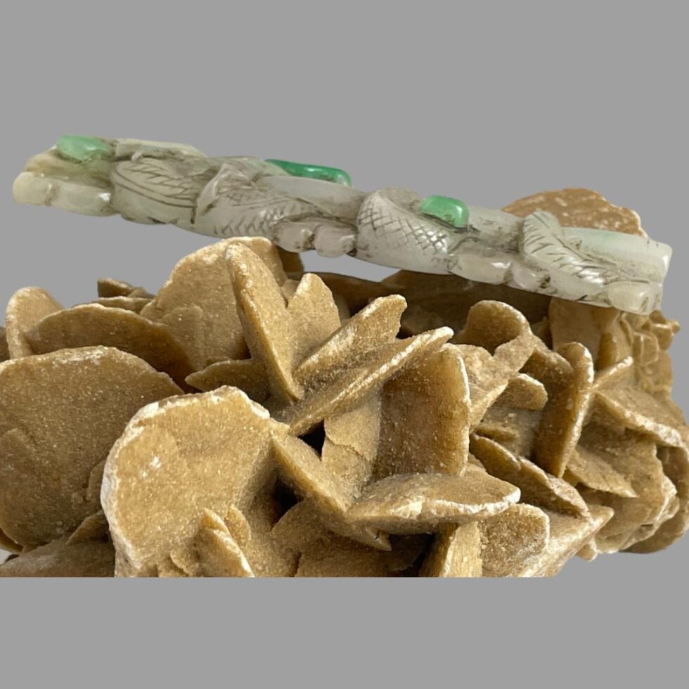 Photo of long jade dragon pendant displayed on top of the rock of desert sand rose and seen from a side angle showing the thickness of the pendant.