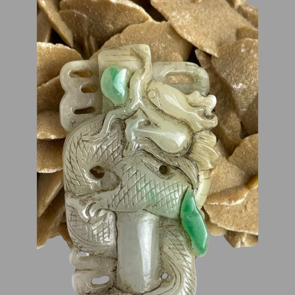 Close up photo of the top part of the long jade dragon pendant showing the dragons head and 2 of the apple green jade inclusions.